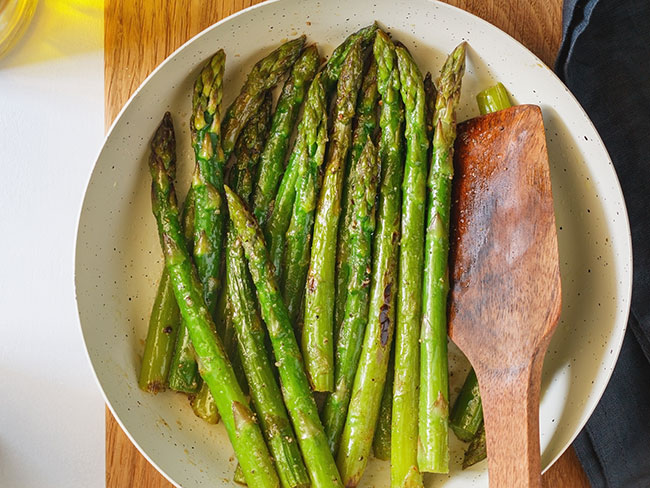 Asparagus with mustard vinaigrette on a white plate on a kitchen table.