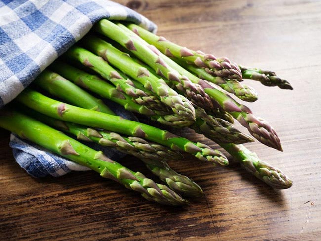 A bunch of fresh asparagus wrapped in a gingham cloth, on a wooden tabletop. 