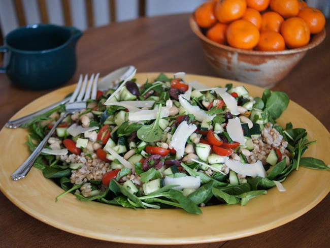 A salad of greens and farro, topped with shaved parmesan, alongside a bowl of tangerines.