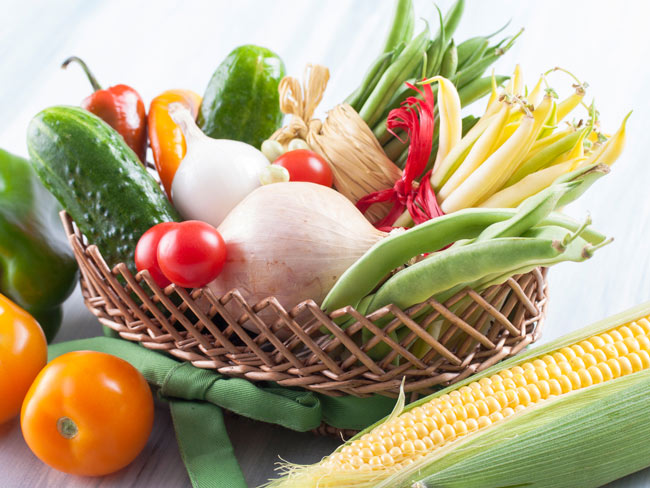 Basket of summer vegetables, including onions, tomatoes, corn, green beans