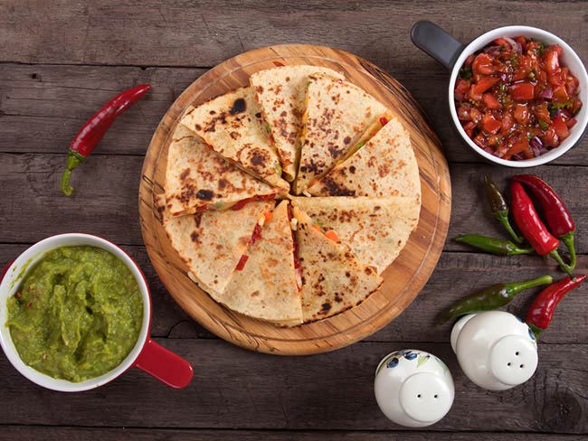 Veggie quesadilla on a round wooden cutting board with salsa and guacamole.