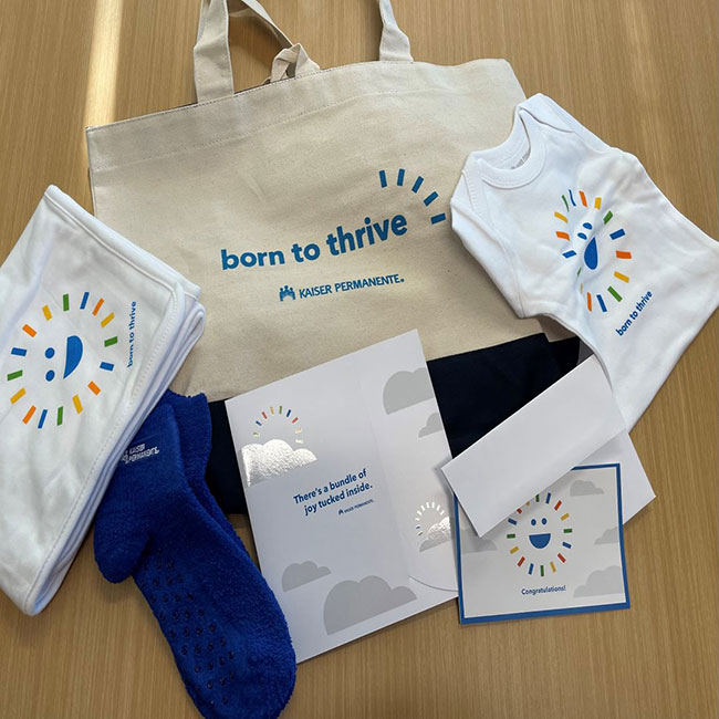 A Kaiser Permanente born to thrive maternity kit, including pregnancy journal, baby onesie, blanket, and  greeting card..