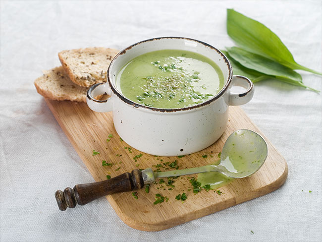 Bowl of green, spring vegetable soup with a ladle and some bread