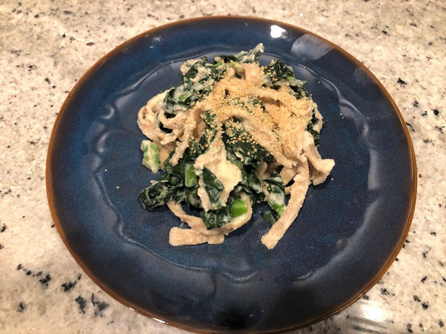 Pasta and greens mixed together on dark blue plate, with breadcrumb mixture on top.