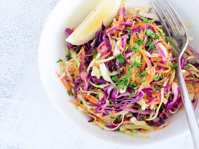 Coleslaw in a white bowl with a lemon wedge