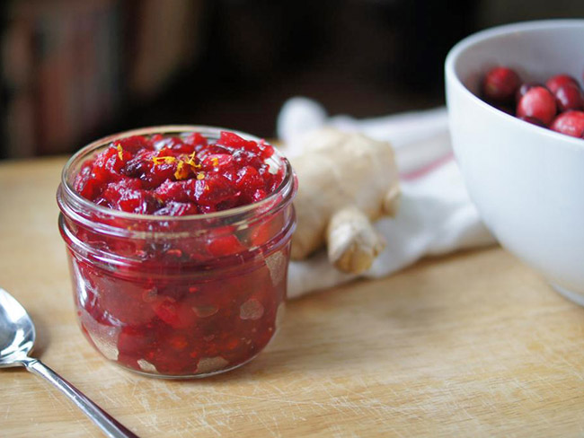 A canning jar filled with homemade cranberry sauce on a wood table top.