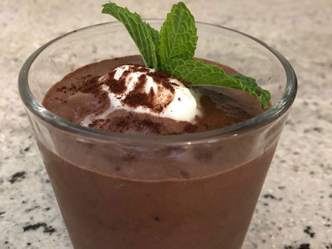 Creamy chocolate shake with frozen banana and mint leaf in glass cup