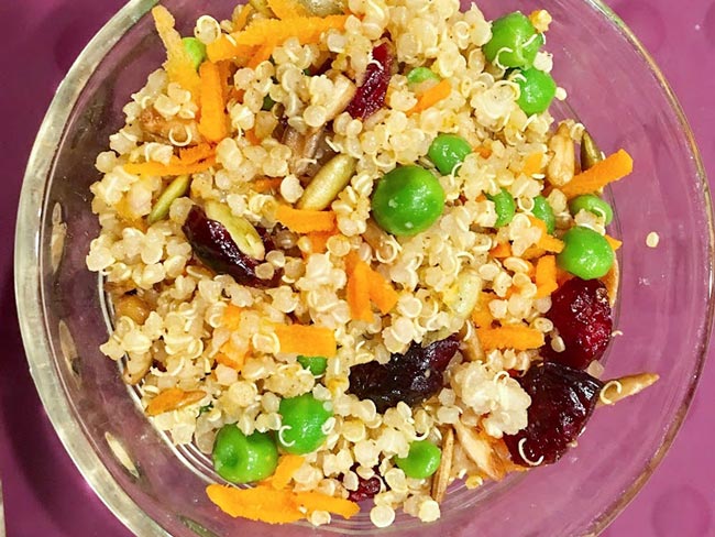 Overhead view of quinoa bowl, including peas, shredded carrots, and other fruits and vegetables