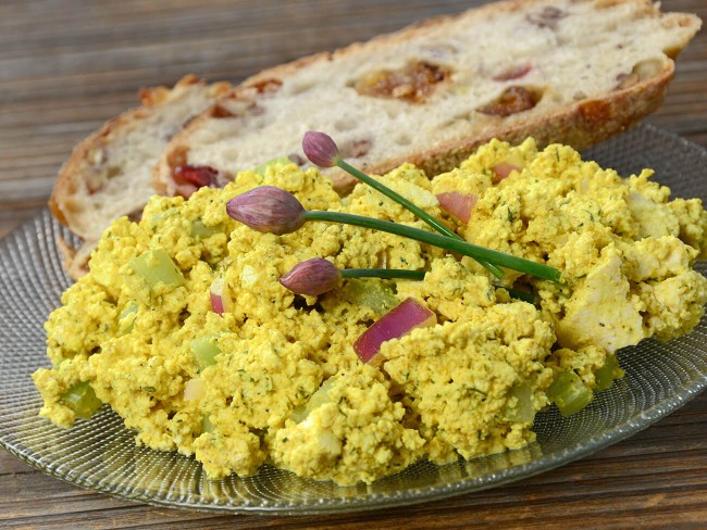 Scrambled tofu mixed with diced vegetables and served with a slice of rustic artisanal bread.