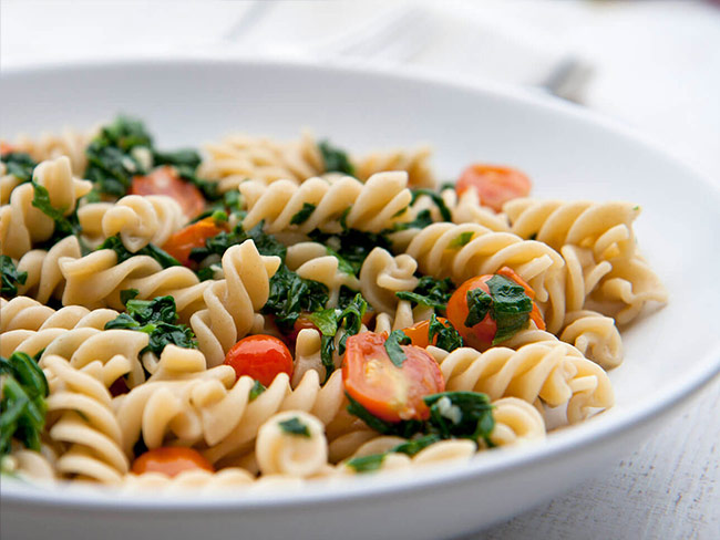 A bowl filled with fusilli pasta salad with tomatoes and arugula.
