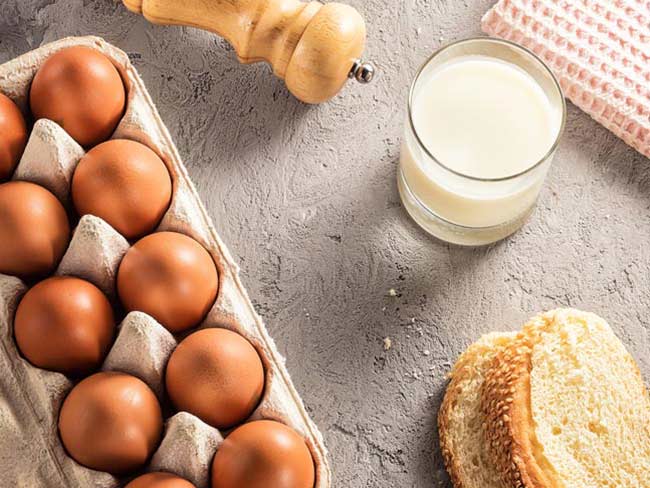 Aerial shot featuring carton of eggs, salt grinder, glass of milk, and bread