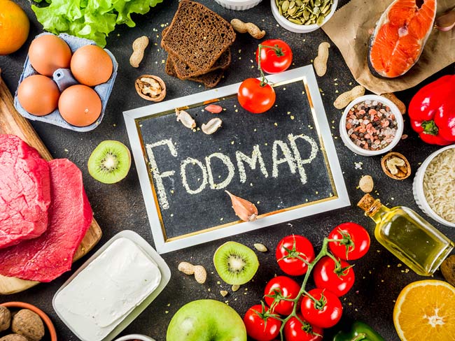 Overhead photo of chalkboard with "FODMAP" written on it in center, surrounded by various foods, including tomatoes and eggs. 