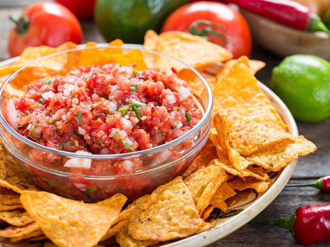 Plate of tortilla chips with small bowl of tomato salsa in the middle.