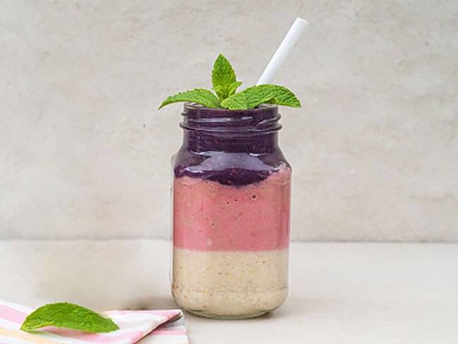 Frozen banana, strawberry, and blueberry smoothie in a mason jar with a straw.