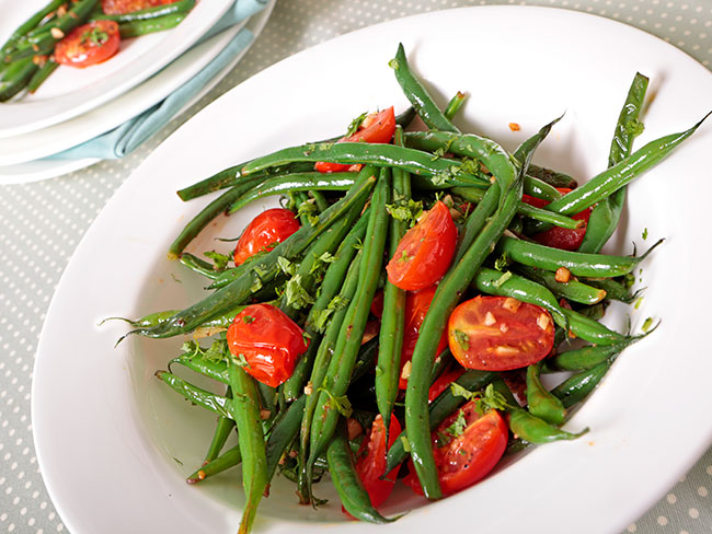 Green beans and tomatoes on white plate.