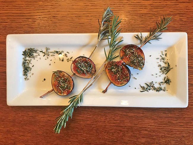 Sliced figs drizzled with honey, on a white plate with sprigs of rosemary.