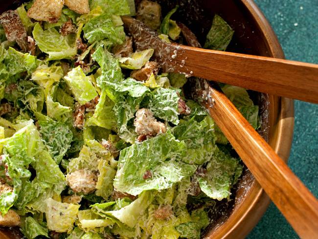 A Caesar salad with croutons in a wooden bowl.