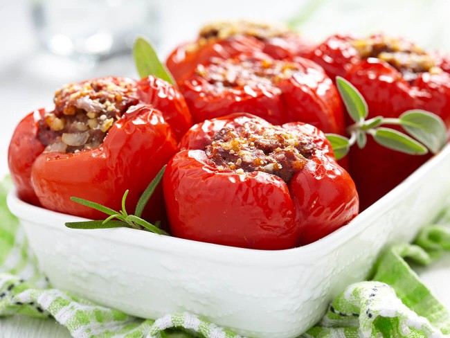 ceramic casserole dish with stuffed red bell peppers garnished with sage leaves