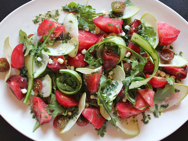 A fresh salad made up of tomatoes, cucumbers and arugula on a plate. 