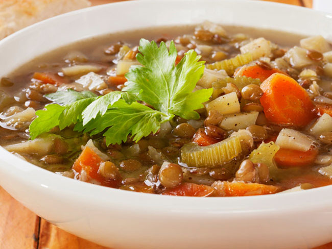 Bowl of soup, featuring lentils, beans, sliced carrots, and vegetables.