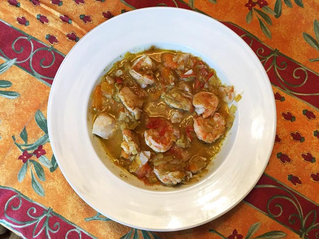 A hearty bowl of Ligurian seafood stew on a multi-colored placemat.
