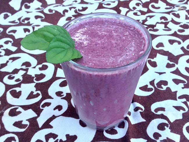A glass of mixed berry smoothie garnished with 2 mint leaves.
