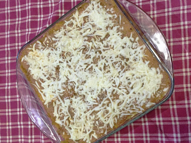 Spaghetti squash lasagna topped with grated mozzarella cheese in a baking dish.