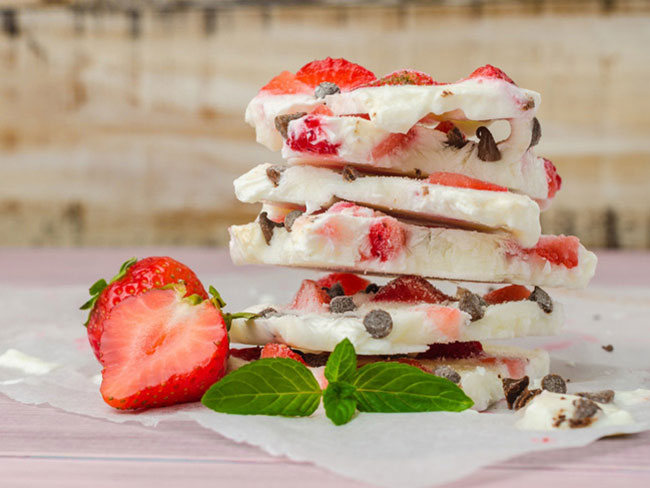 Stack of frozen yogurt bark with strawberries and chocolate chips on each piece.
