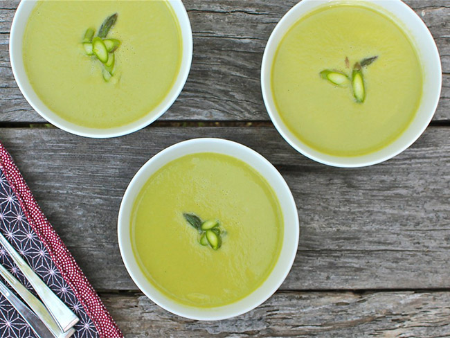 Top down view of 3 bowls of asparagus soup, each topped with slivers of asparagus for garnish.