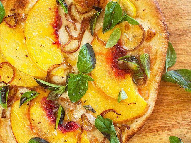 A pizza topped with baked peaches, onions and sprigs of basil.