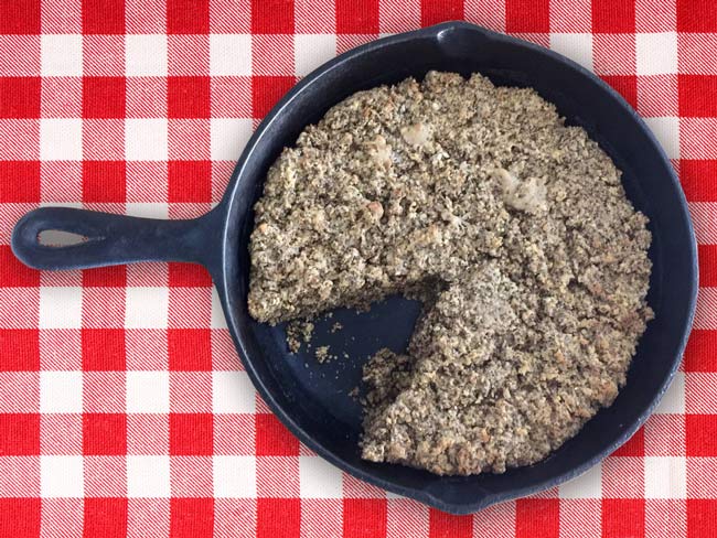 Overhead picture of nutty cornbread in cast-iron skillet on red checkered table cloth.