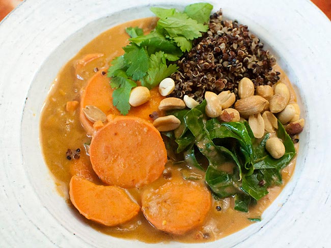 Bowl of soup with sweet potato rounds, collard greens, quinoa, peanuts and cilantro