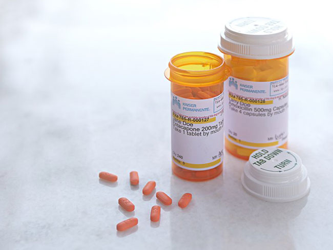 Two prescription bottles on a white surface. One is open and several pills are laid out in front of it. 