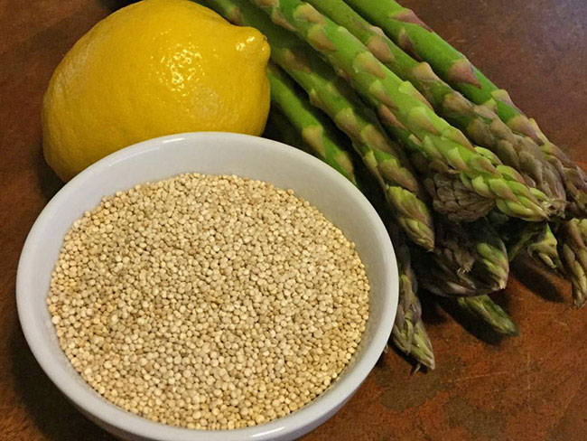 bowl of dry quinoa placed next to a large ripe lemon and a bunch of asparagus spears