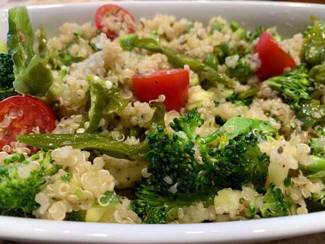 Broccoli, tomatoes, and Shishito peppers on top of quinoa in bowl