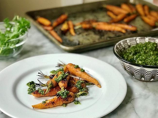 Roasted carrots with carrot top and cilantro pesto on a white plate.