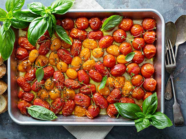 Roasted cherry tomatoes with herbs in a baking pan.