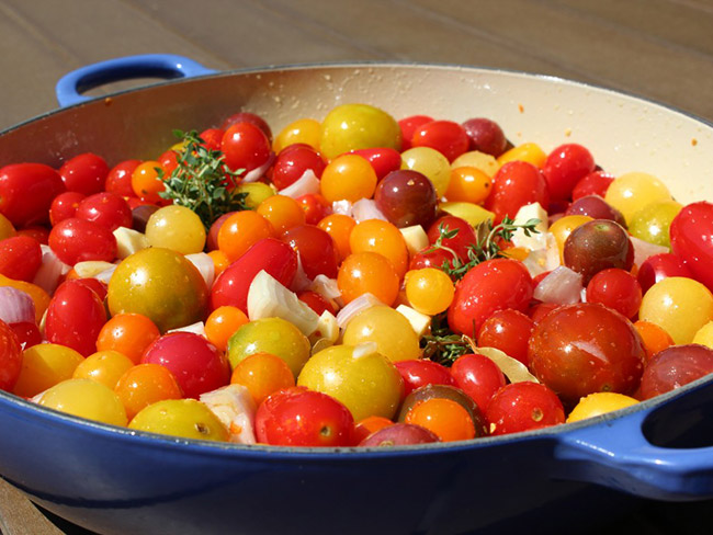A blue skillet filled with an assortment of cherry tomatoes, shallots and sprigs of fresh thyme. 