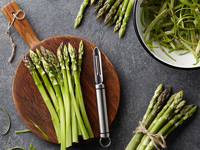 Shaved raw asparagus on a wooden cutting board