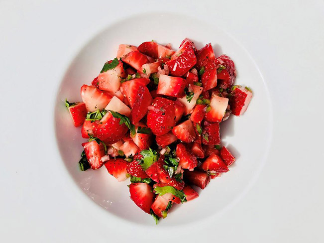 A white bowl filled with fresh strawberry salsa.