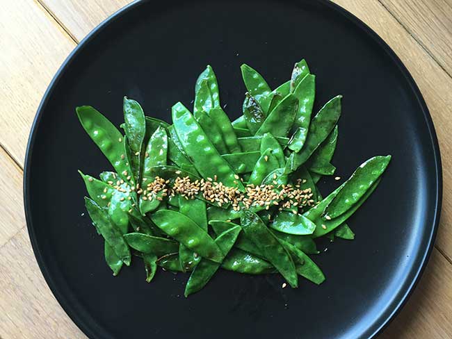 Snap peas dusted with sesame seeds on a black plate