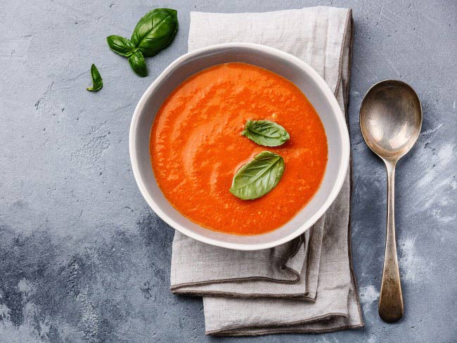 A hearty bowl of creamy tomato soup, topped with two oregano leaves.
