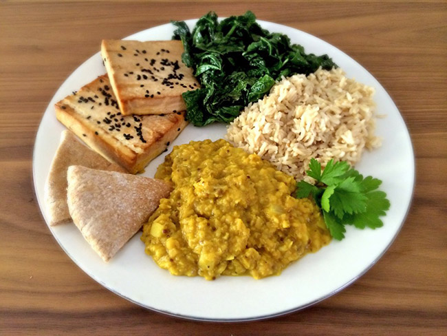 Plate arranged with grilled tofu, sauteed kale, brown rice, lentil dal, and pita bread
