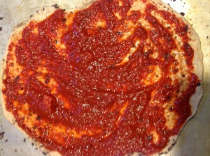 Homemade pizza crust topped with tomato sauce.