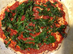 Homemade pizza crust topped with sauce and cooked chard.