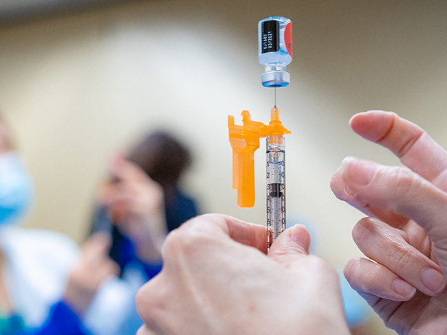 close-up of hand holding a syringe with a vial of COVID-19 vaccine
