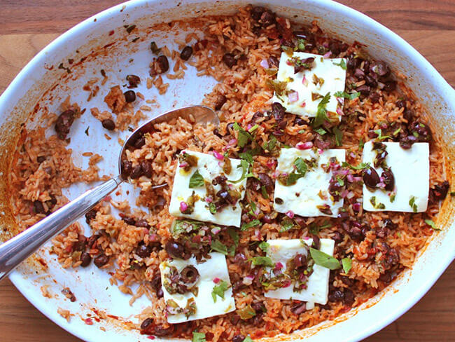 Veracruz-style baked rice and beans, topped with slices of feta cheese in a white baking dish.