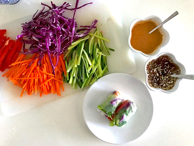 Vietnamese fresh spring rolls with rainbow vegetables and tofu on a white plate with assorted julienned vegetables on the side.
