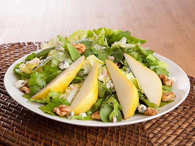 Walnut, pear, and blue cheese salad on a white place sitting on a wicker placemat.