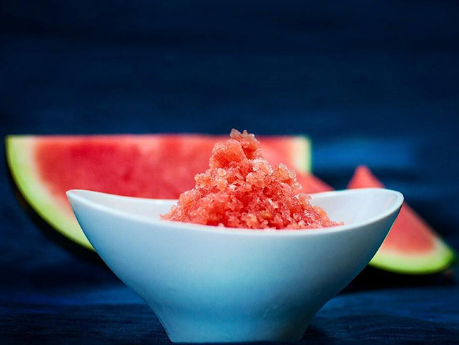 Watermelon granita in a white bowl, with a sliced watermelon in the background.